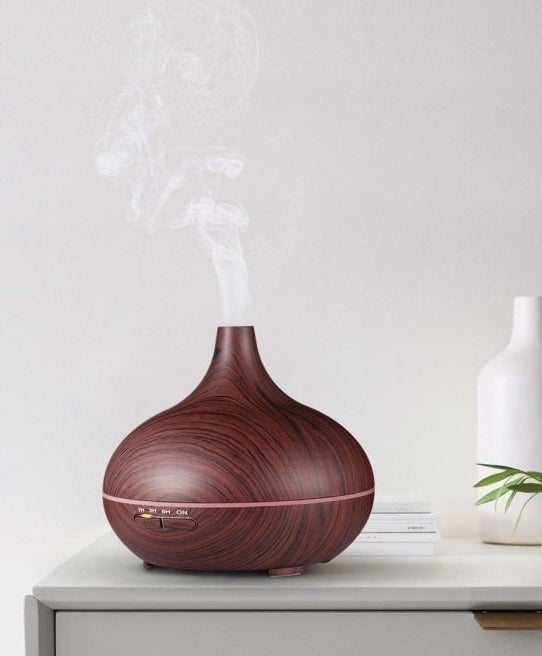 The diffuser in brown with a wood-like pattern sitting on a table releasing steam into the air