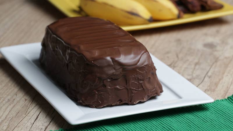 Você vai precisar de:1 kg de banana passa picada1 xÃcara de água½ xÃcara de leite condensado2 xÃcaras de chocolate ao leite derretido, divididas¼ xÃcara de creme de leiteModo de preparo:1. Forre uma forma de bolo inglês de 10x20cm com um saco plástico ou plástico filme e reserve.2. Em uma tigela grande, adicione as bananas e a água e leve ao micro-ondas por 4 minutos.3. Em um processador, adicione as bananas quentes, o leite condensado e bata até obter uma massa homogênea.4. Espalhe a massa de banana na forma preparada e em seguida, leve ao congelador por 1 hora.5. Em uma tigela média, misture 1 xÃcara de chocolate derretido com o creme de leite e misture até ficar homogêneo.6. Desenforme a massa de banana e cubra com o ganache de chocolate. Leve ao congelador até endurecer, por cerca de 10 minutos.7. Coloque a massa de banana gelada em uma grade sobre um prato. Despeje a xÃcara restante de chocolate derretido sobre o bombom até cobrir completamente, em seguida, espalhe uniformemente. Leve à geladeira por cerca de 5 minutos para endurecer.8. Fatie e sirva.9. Aproveite!
