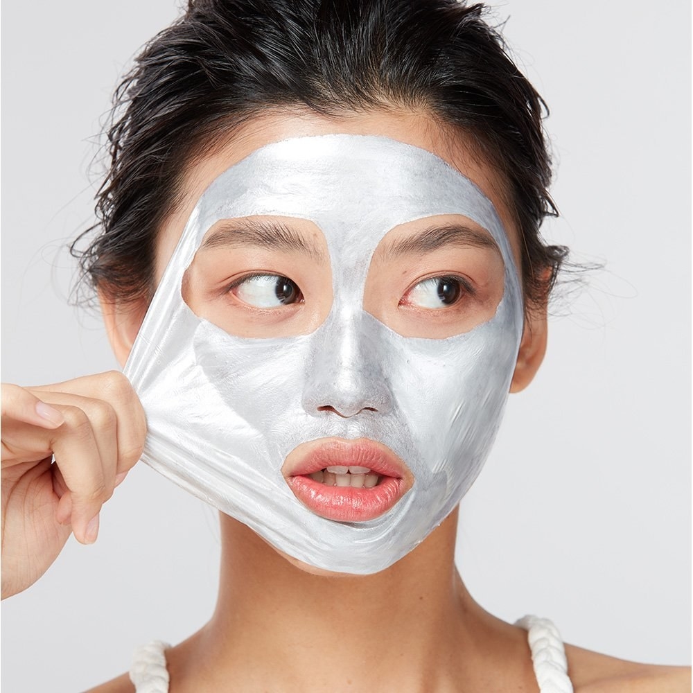 a model beings to peel off a metallic silver mask