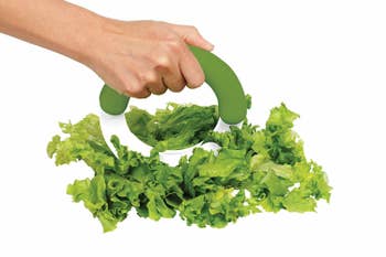 A hand rocking the chopper on a pile of lettuce 