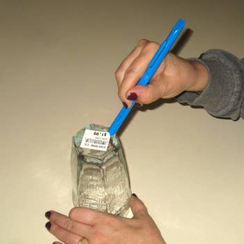 a pair of hands using the scratch-free scraper tool to remove a label from some glassware