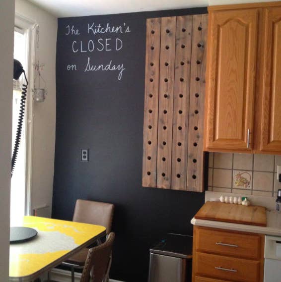 A kitchen wall painted with the chalkboard paint, with the words &quot;The Kitchen&#x27;s CLOSED on Sunday&quot; written in chalk