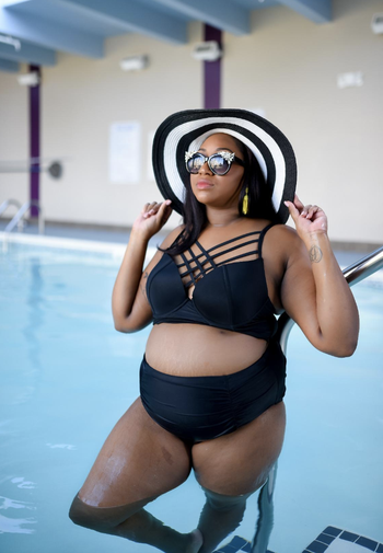 a reviewer wearing the bathing suit in black it has an array of criss crossed straps on the top and a high waisted bottom