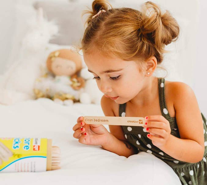 Child holding up large popsicle stick that says &quot;clean bedroom&quot; 