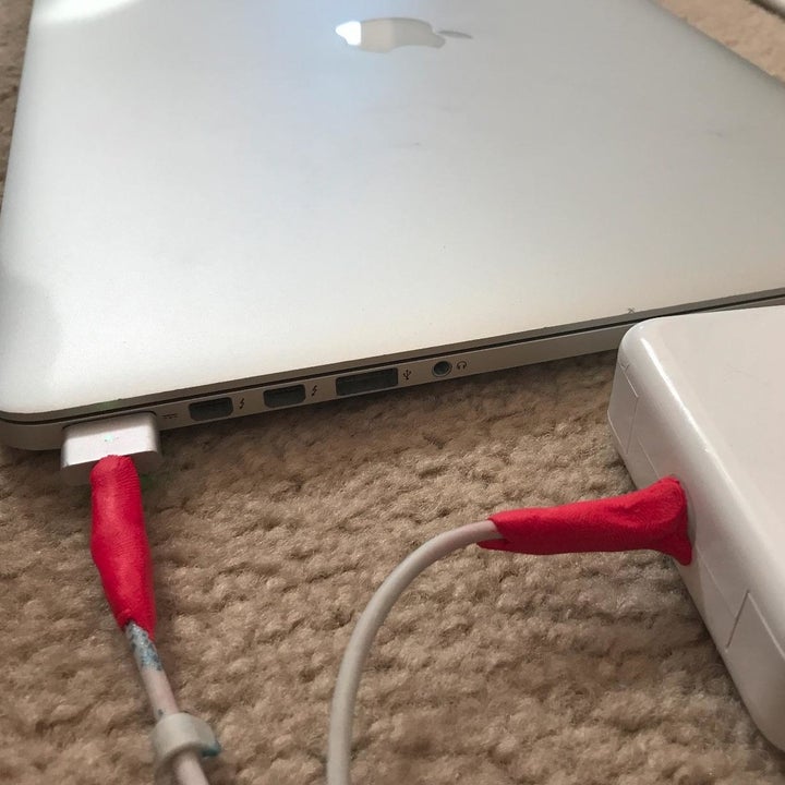 A reviewer photo of a laptop charging cord with red mouldable glue applied to each end to fortify the cord 