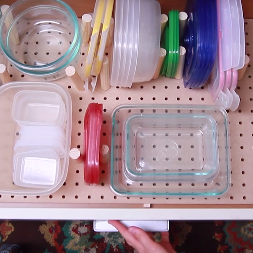 Kitchen drawer pulled out with wooden pegs on a peg board, organizing a bunch of containers and lids