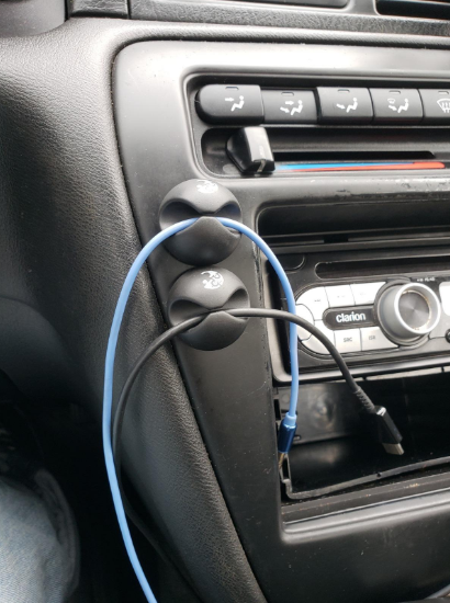 Two cable clips attached to the dashboard of a car holding two charging cords off the ground