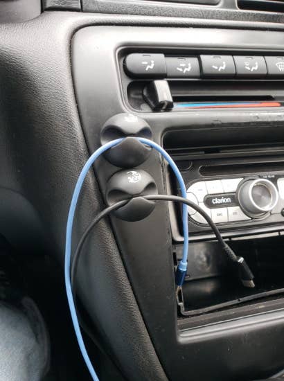 Reviewer photo of the clips mounted to a car dashboard holding two charger cables in place 