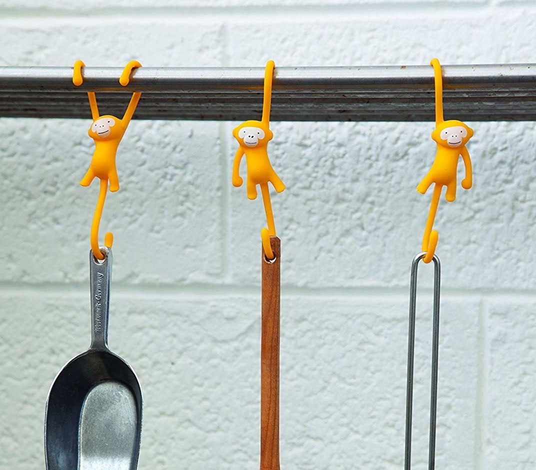 three monkeys hanging on pole with curved tails that hold pots
