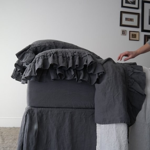 a hand reaching towards a bed made with the gray ruffly sheets 