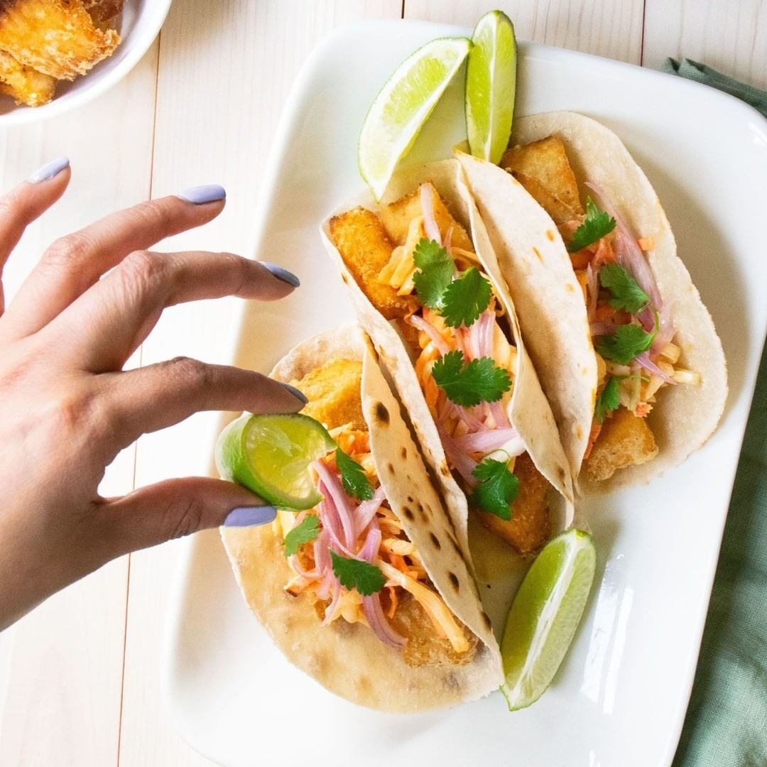 a hand squeezing a wedge of lime onto three tacos on a plate