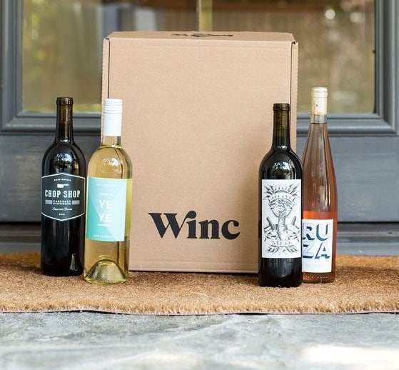 a &quot;winc&quot; box on a doorstep with two bottles of red wine, one bottle of rosé, and one bottle of white wine