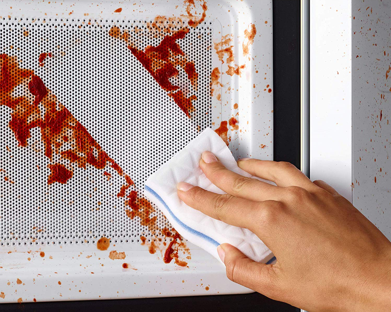Hand wiping tomato sauce off microwave 