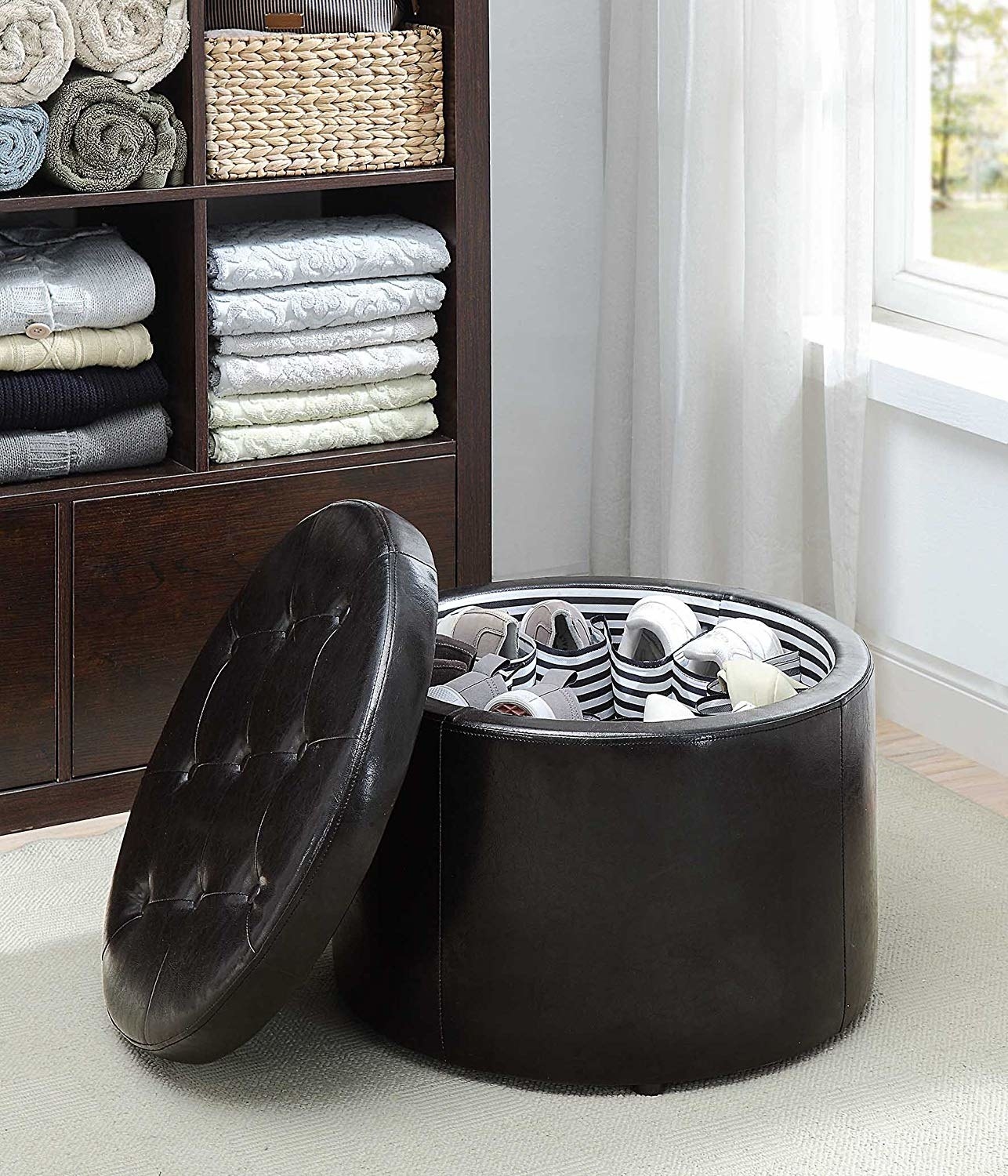 Circular faux-leather ottoman with the tufted lid next to it and striped fabric cubbies with shoes in inside of it
