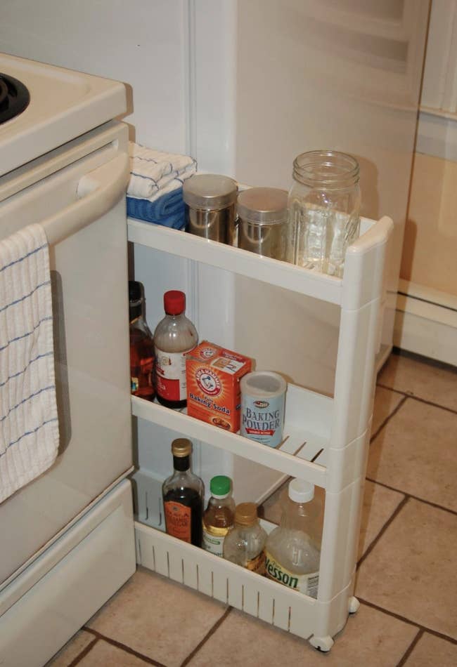 reviewer image of the white tower between an oven and a fridge with assorted kitchen products on each shelf