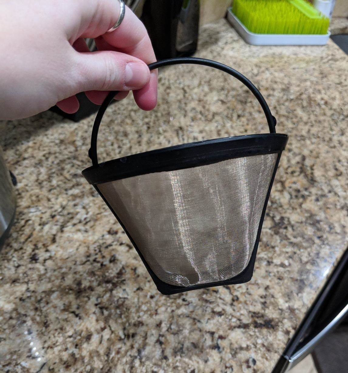 someone holding a fine mesh reusable coffee filter by its black plastic handle