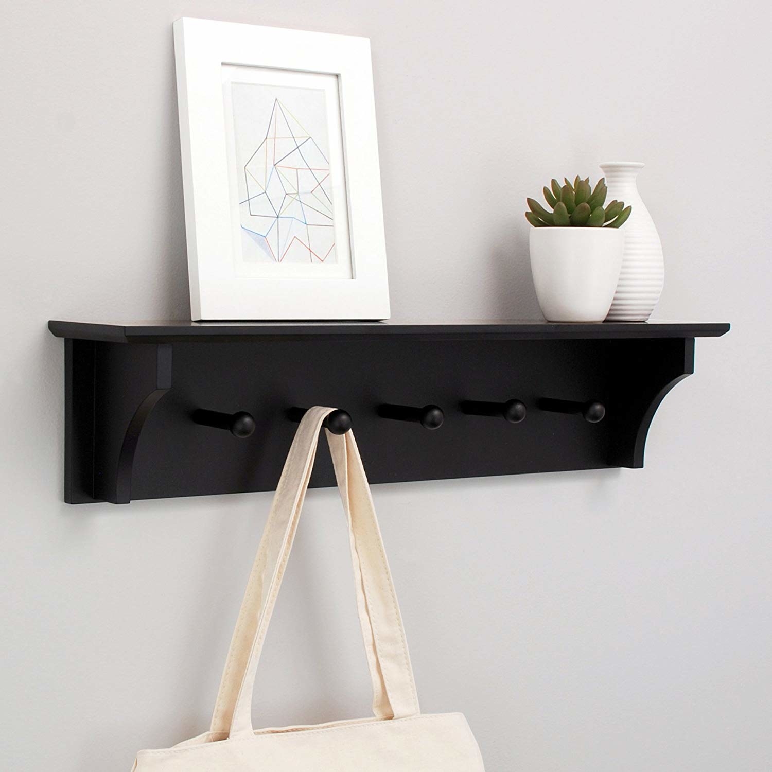 black wall shelf with five pegs hanging on the wall