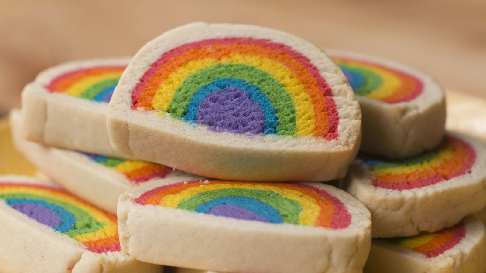 Makes: 24 cookies INGREDIENTS1 cup butter, softened2½ cups powdered sugar1 teaspoon vanilla1 pinch salt3 eggs3½ - 4 cups flourRed, orange, yellow, green, blue, and purple food coloring PREPARATIONPreheat oven to 350˚F/180˚C.Using a hand mixer or standing mixer, beat butter until creamy.Add powdered sugar and beat until combined. Add the vanilla, salt, and eggs. Beat until well combined.Gradually, add the flour until dough is moist and holds together, but doesn’t stick to your hands.Place dough on a cutting board and form into a ball. Cut in half, then cover one half with plastic wrap and set aside. Divide the other half into 6 pieces. The outer layers of the rainbow will need a little bit more dough, so make two of them slightly larger than the others.Dye the dough with food coloring by placing a ¼ teaspoon of dye on the ball of dough and kneading it until it is one solid color. Gloves optional but suggested.Starting with purple, roll the dough into a log about 6-8 inches long. This will be the center of the rainbow. Next, roll out the blue dough with a rolling pin until it’s about ¼ inch thick, slightly longer than the purple, and wide enough to wrap around the purple dough. Repeat with the green, yellow, orange, and red doughs. The further away from the purple you get, the wider the dough needs to be to go around the previous color, making the red dough the widest.Wrap the blue dough around the purple, pinching together any cracks that form, cutting off any excess dough. Repeat with the rest of the colors. Wrap in plastic wrap and chill for 30 minutes.Once chilled, remove the plastic wrap, and cut the dough in half to make 2 rainbow shapes. Set aside.Cut the reserved dough in half, roll out to ¼-inch thickness, and make it slightly longer than the rainbow log. Place the rainbow dough in the center and wrap the plain dough around it, again, pinching together any cracks and smoothing out the surface. Repeat with the other halves. Wrap with plastic wrap and chill for another 30 minutes.Slice cookies about ½-inch thick and place on a parchment paper-lined baking sheet.Bake for 20 minutes or until the bottom has browned slightly.Cool on a cooling rack.Enjoy! Inspired by Heather Baird https://blog.etsy.com/en/show-your-pride-with-diy-rainbow-cookies/?geo=global