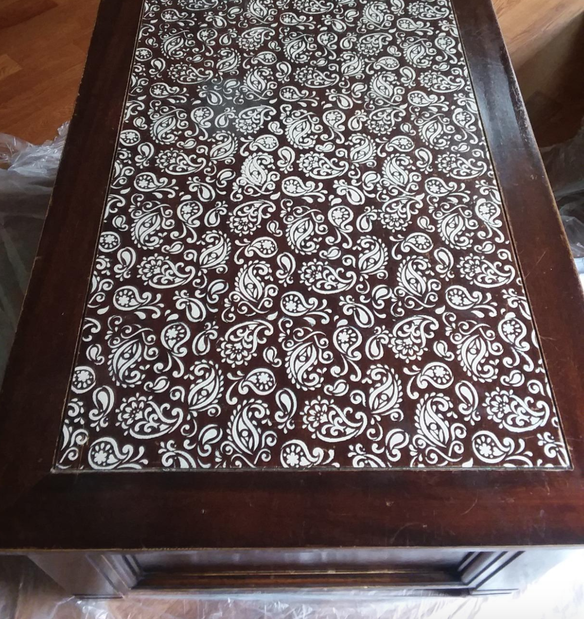 A wood coffee table with the stenciled white paisley pattern on top