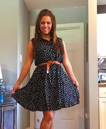 reviewer wears black dress with cat print and brown belt 