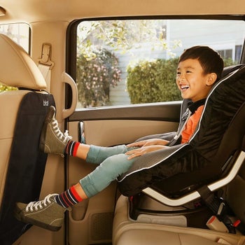A kid in a backseat of a car with their feet kicking the front seat but the cover is protecting the back of the car seat
