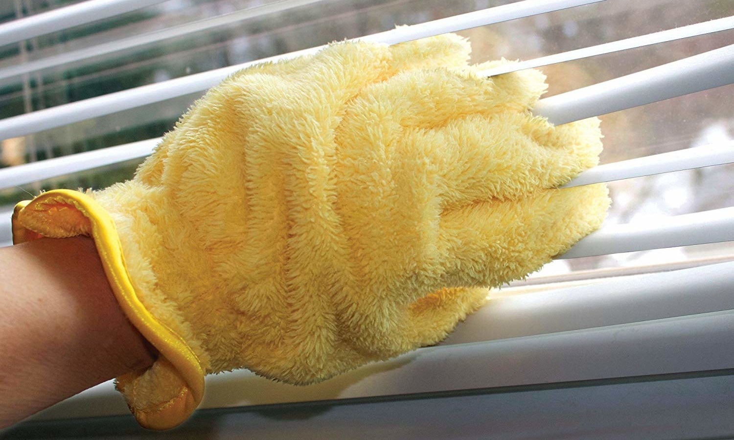 a hand wearing a yellow dusting glove and using it to clean window blinds