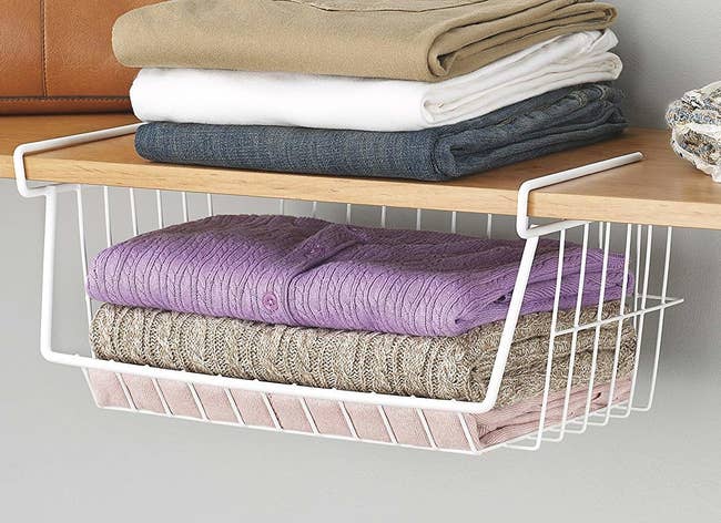 white wire basked attached below a shelf with sweaters in it