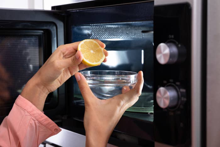 A bowl of water with a lemon half going into the microwave
