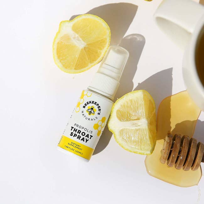 small spray bottle of product beside cut lemon and dripping honey 