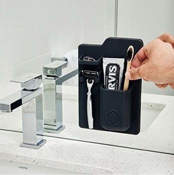 A hand reaching to pull a toothbrush out of the black toiletry holder
