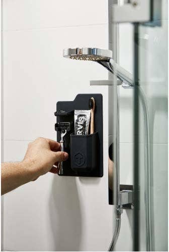 A hand reaching to place a razor in the black toiletry organizer