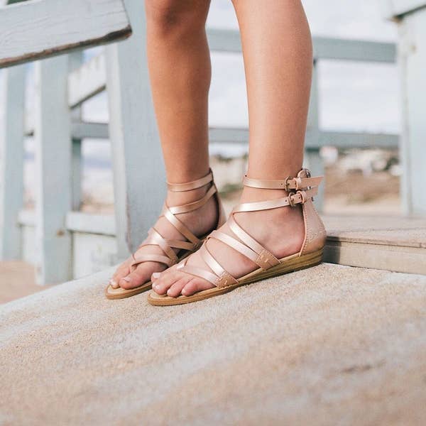 person wearing rose gold color sandals in a beach-y setting