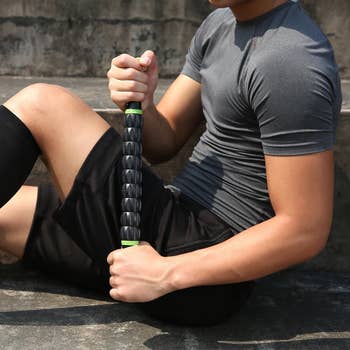 person using the black muscle roller stick on their thigh