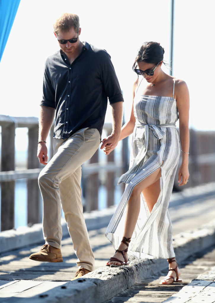 Meghan and Harry walking on a boardwalk wearing casual clothes and sunglasses