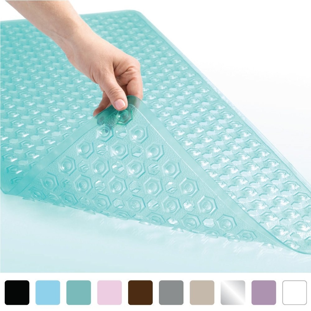 a hand peeling back the bath mat with the colors of the mat below 