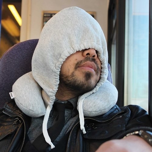 A model covering their face with the hoodie while using the pillow on a train