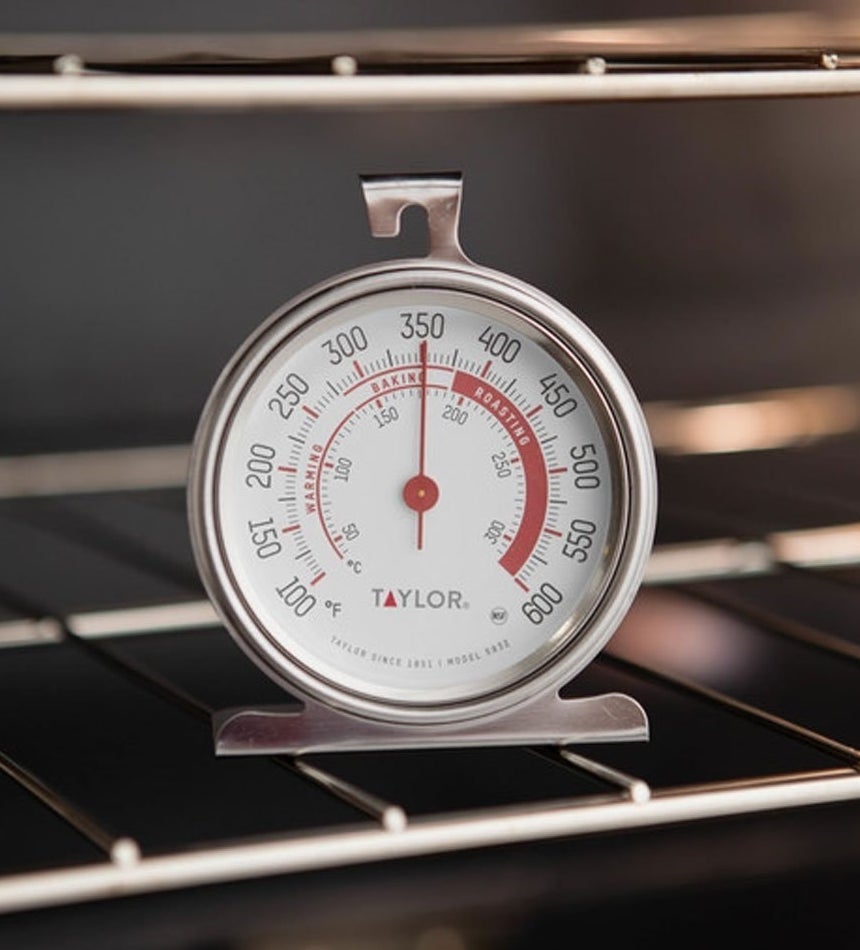 A round thermometer with top hook and stand sitting on an oven rack