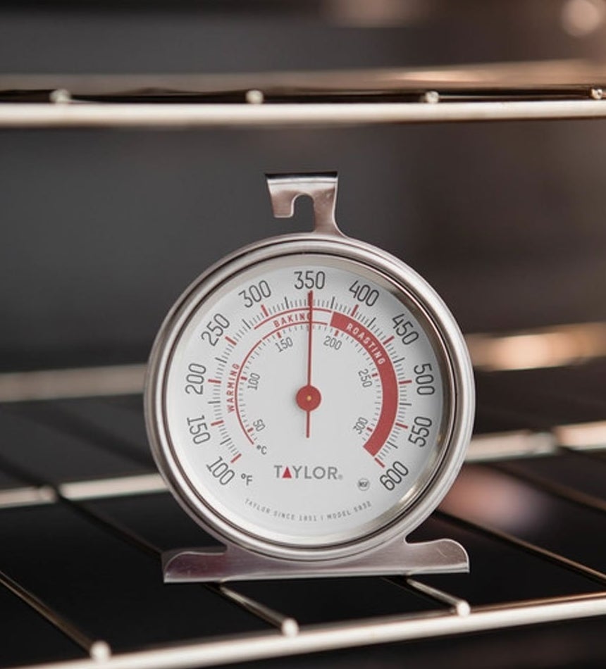 A round thermometer with top hook and stand sitting on an oven rack