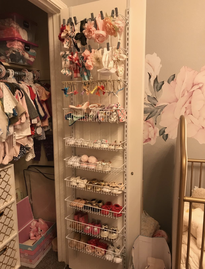 Reviewer photo of the shelving unit on the back of a closet door filled with seven shelves filled with baby shoes and three rods with bows and head pieces 