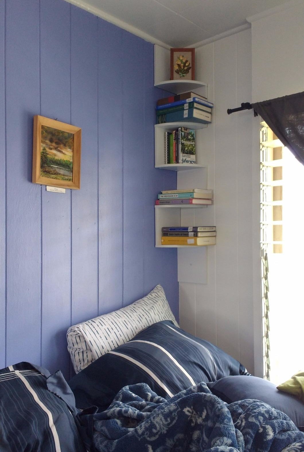 a reviewer photo of three of the white shelves in a corner of a bedroom with books on them