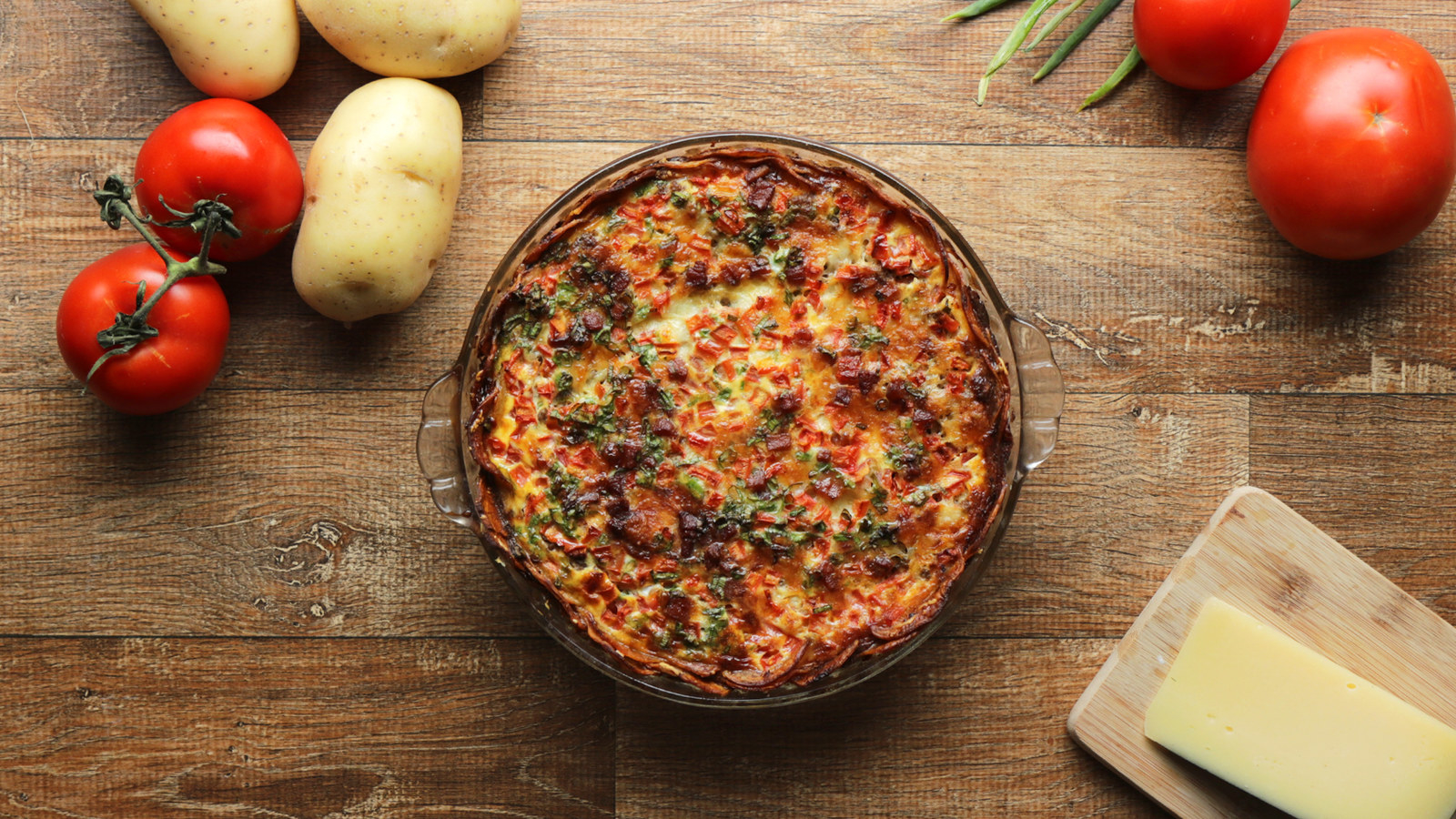 . Pré-aqueça o forno a 180°C (350°F).2. Fatie as batatas em uma mandolina ou com uma faca afiada.3. Em uma tigela média, adicione as batatas cortadas, o queijo parmesão, a pimenta, 1 colher de chá de sal e o azeite. Misture com as mãos para cobrir as batatas.4. Organize as fatias de batata em uma travessa refratária de 22 centímetros, começando no centro e finalizando para fora, sobrepondo ligeiramente as fatias.5. Asse as batatas por cerca de 15 minutos, ou até ficarem macias, mas não douradas.6. Em uma tigela média, misture os ovos, a cebolinha, o leite e a colher de chá de sal restante. Bata até ficar homogêneo.7. Cubra a base de batata com a carne moída, a muçarela, o bacon e o tomate. Despeje uniformemente sobre a mistura de ovos. Se alguma das fatias de batata começar a flutuar, use uma colher para colocá-las de volta no lugar.8. Asse a torta por 30 minutos, ou até que os ovos estejam firmes e as batatas estejam douradas.9. Fatie e sirva.10. Aproveite!