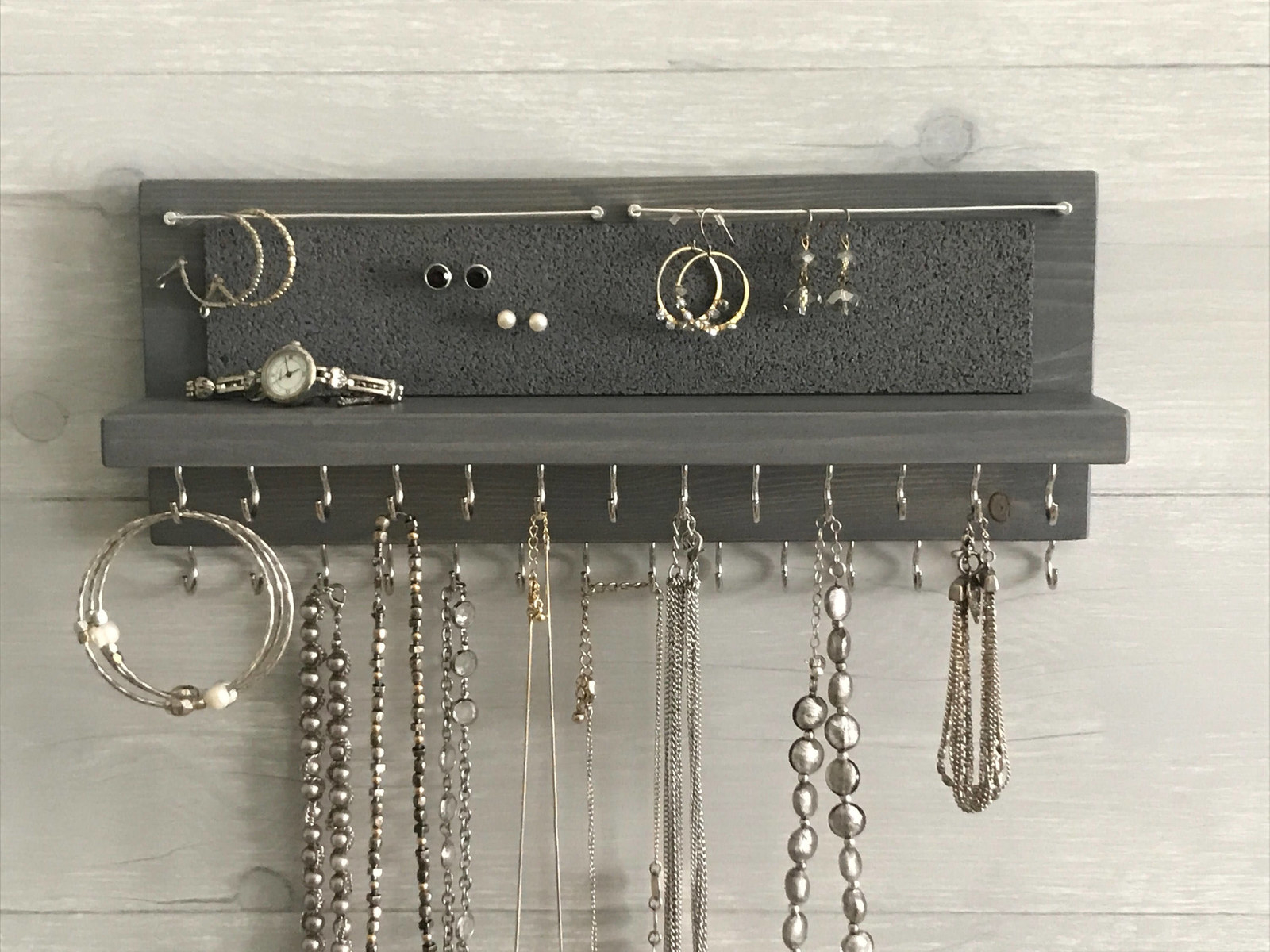 wood organizer with small shelf, cork section for stud earrings, wire section for dangle earrings, and two rows of 13 hooks for necklaces and bracelets