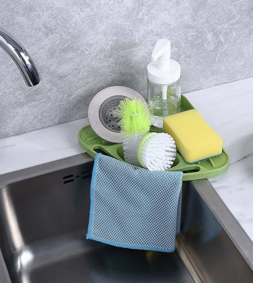 the triangle-shaped green corner tray with drainage area for sponge and soap, over-sink slot for scrub brushes, and small bar to hang dishcloth