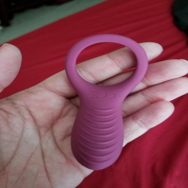 A reviewer photo of a hand holding a pink vibrator with an attached cock ring 