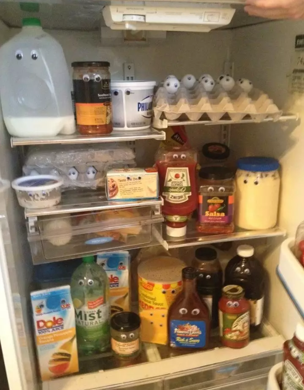 An open fridge stocked with various food items, including cartons and bottles with googly eyes