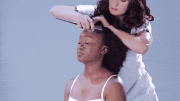 A gif of a model&#x27;s curly hair being pulled up into three hair ties to create a fauxhawk effect
