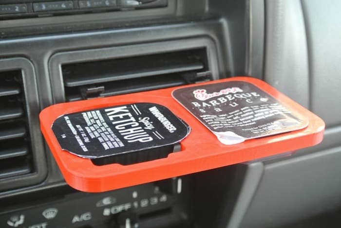 a red contraption clipped into a car vent holding fast food ketchup and barbeque sauce containers