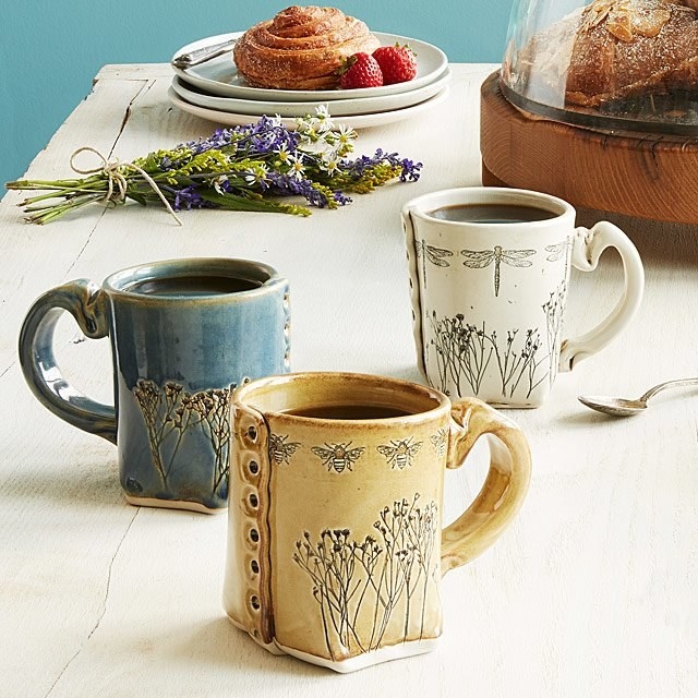 a yellow, blue, and white mug with wildflowers pressed into them 