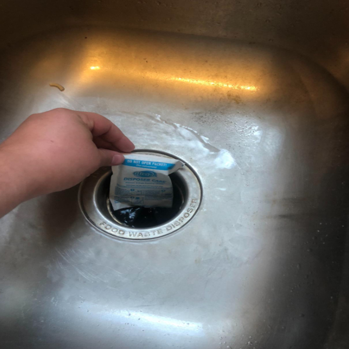 A reviewer's hand inserting the packet in their garbage disposal