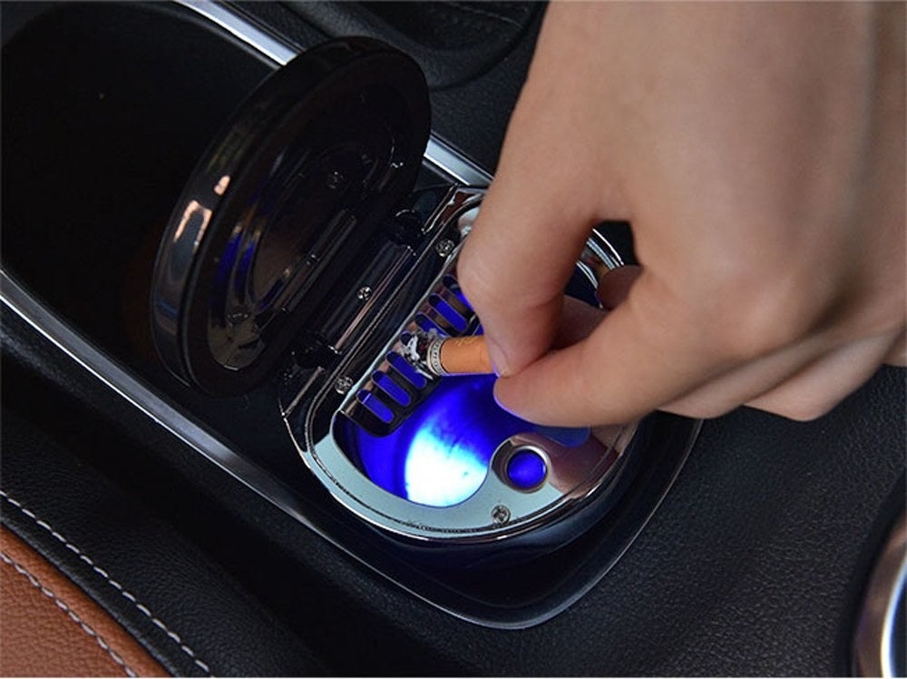 person putting their cigarette out in a light-up ash tray that fits in a car cup holder